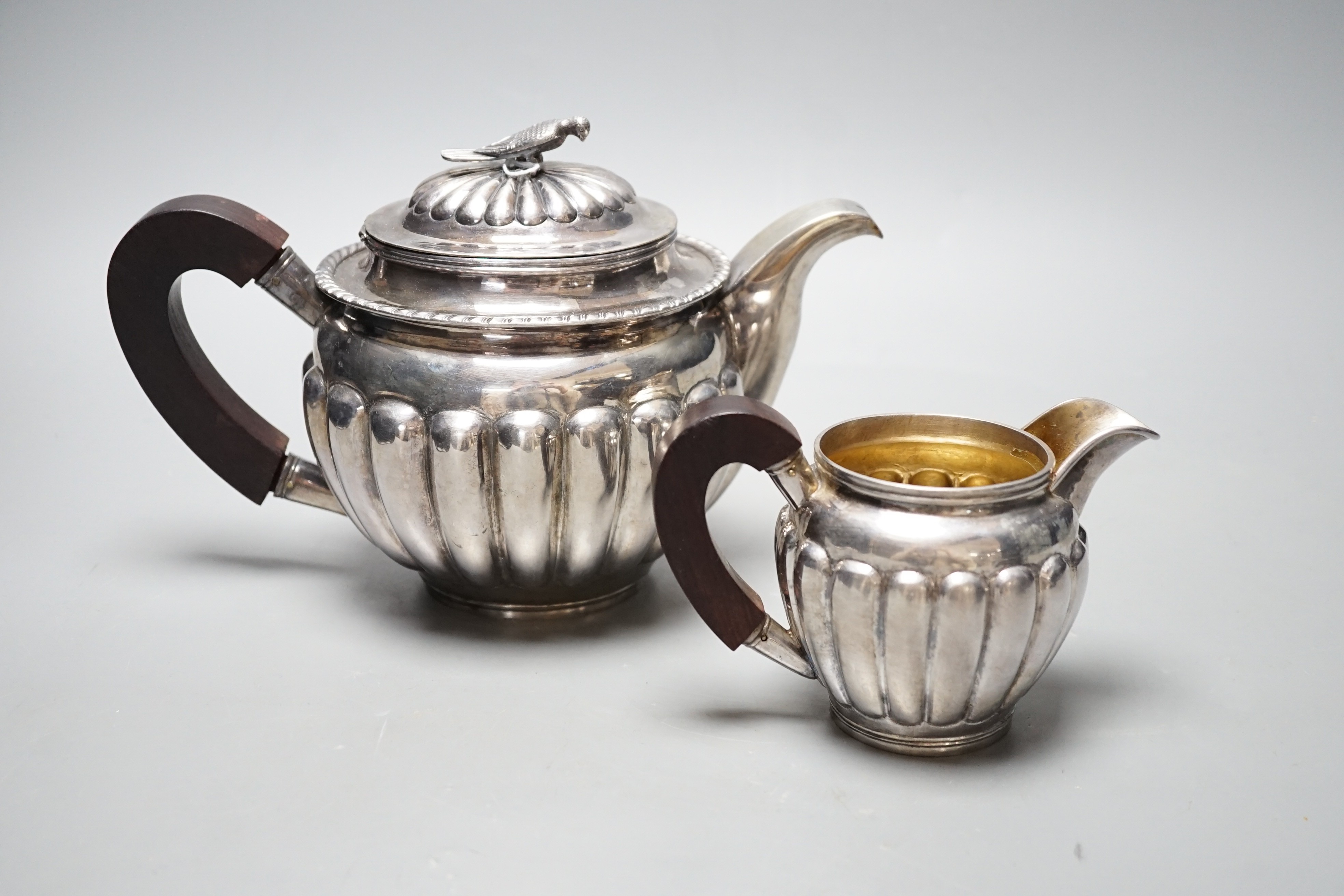 A Chinese Straits? demi fluted white metal teapot and cream jug, with rosewood handles and bird finial, maker TAI, gross weight 31.5oz.